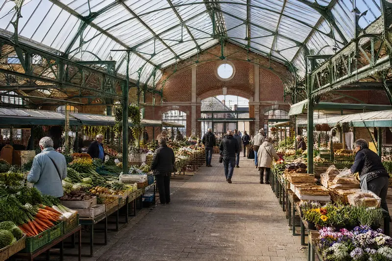 La halle un samedi matin : charpente métallique verte, étals de légumes, de fleurs et de pain.
