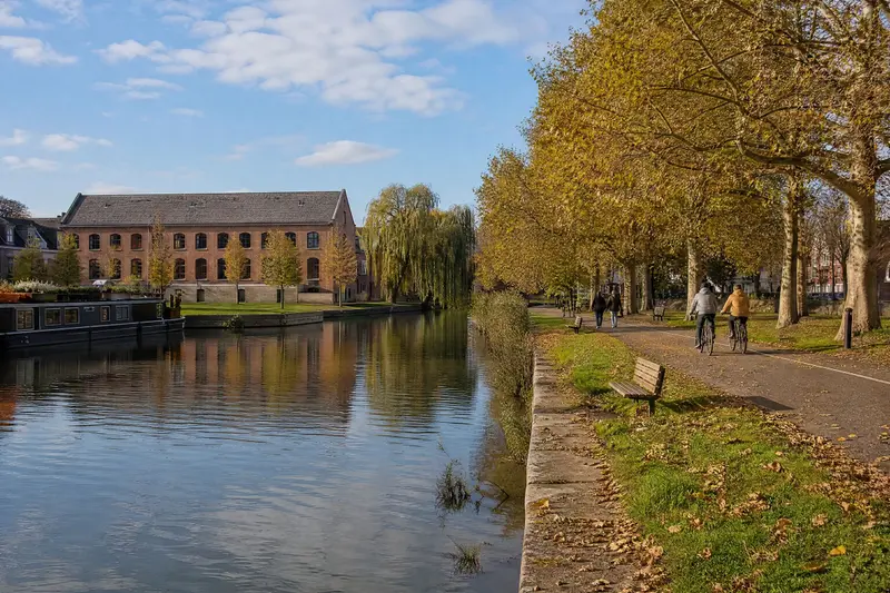 The canal park: stone quays, a tree-lined towpath with cyclists and a brick warehouse in the background.
